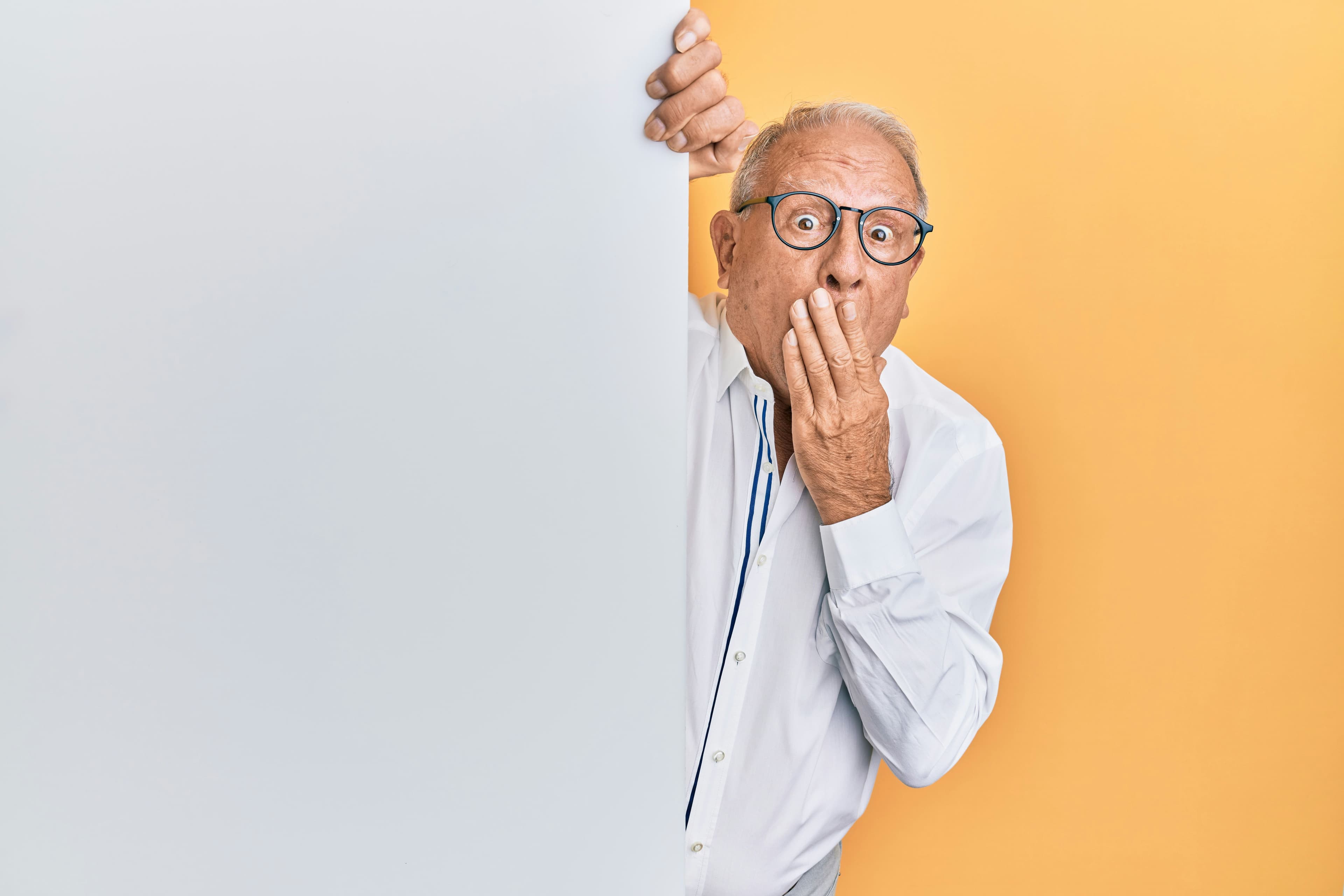 an elderly man is holding a white sign and covering his mouth with his hand .