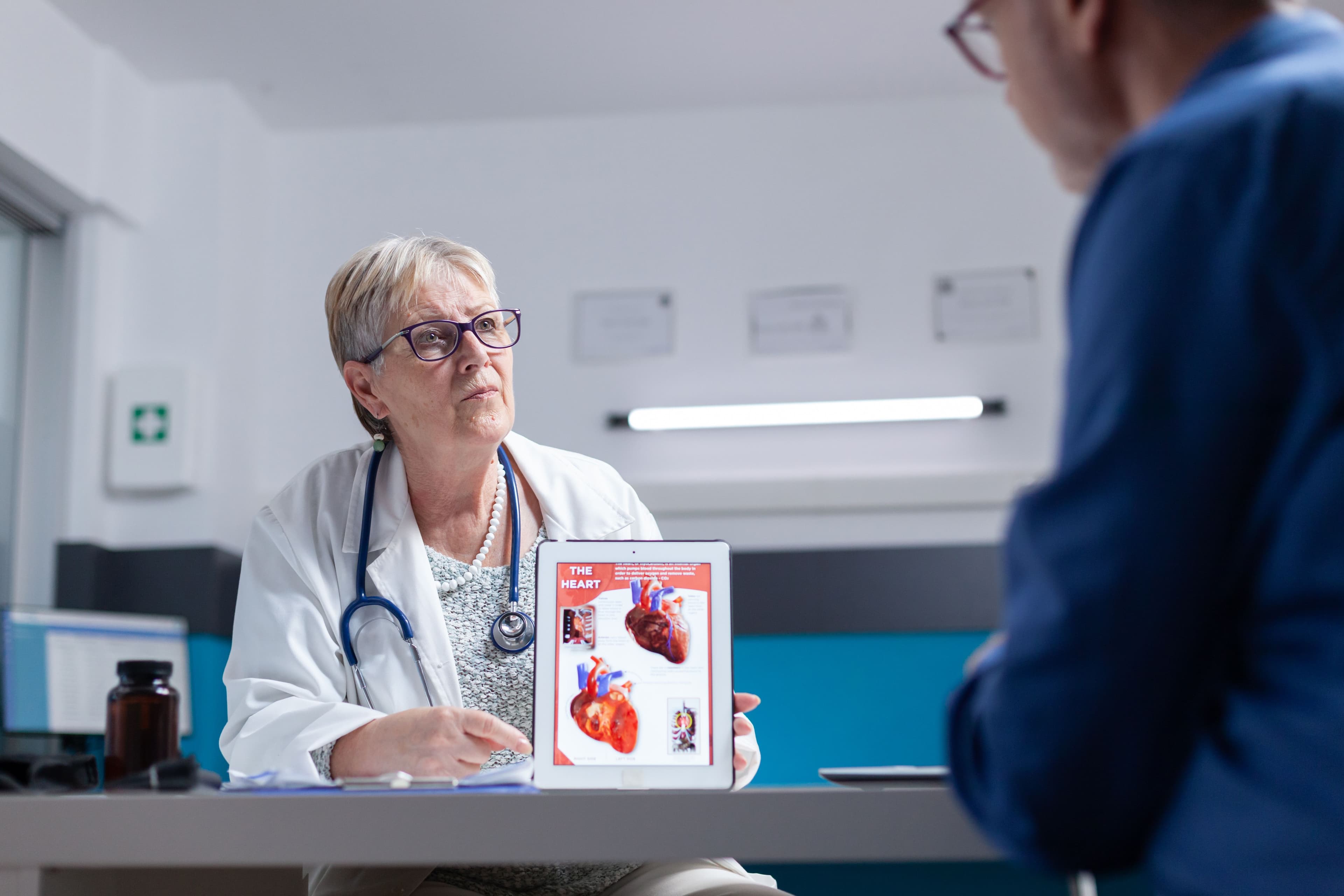 a doctor is holding a tablet with a picture of a heart on it while talking to a patient .