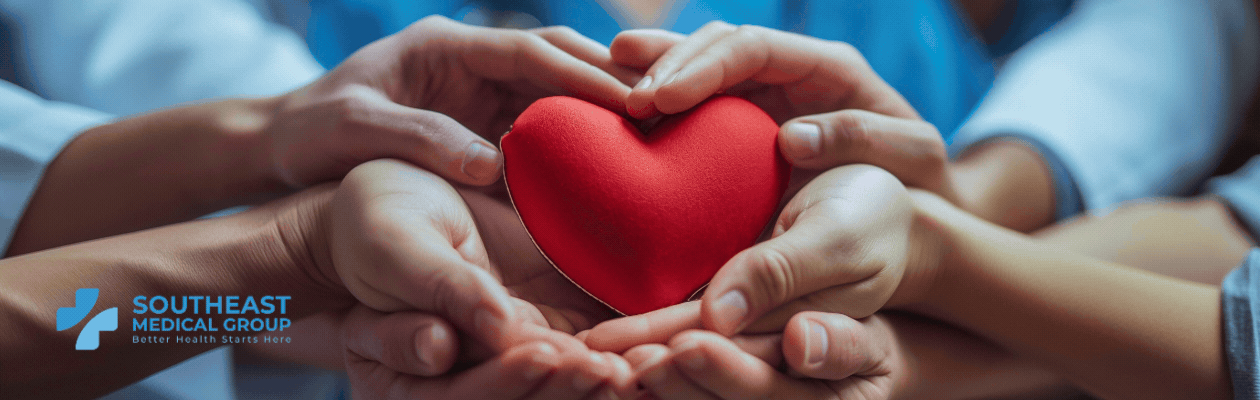 Multiple hands, including a child's and a medical professional's, cradling a red heart. Southeast Medical Group logo in the corner.