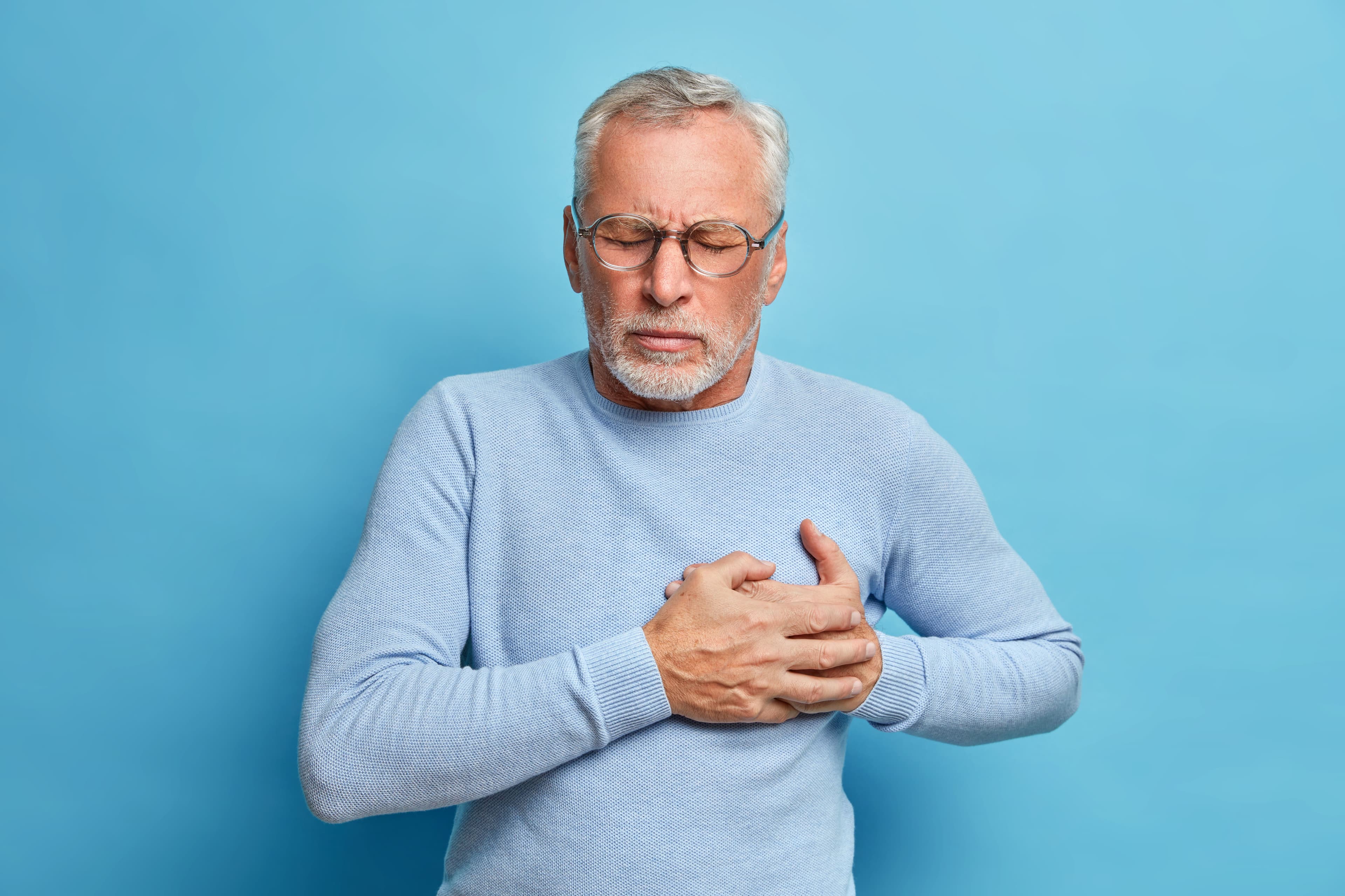 Valvular Heart Disease: a man with glasses is holding his chest in pain .