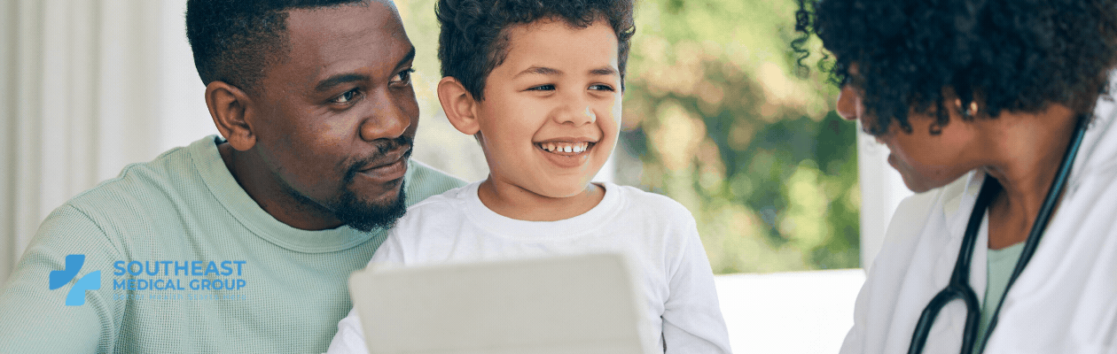 A Black father and his smiling son look at a tablet with a Black female doctor. Southeast Medical Group logo.