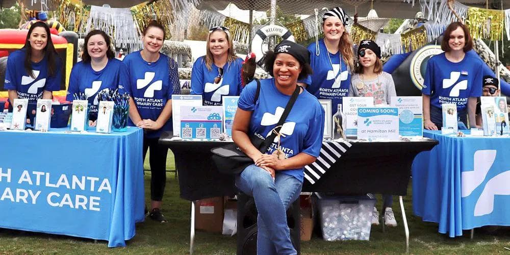 a group of women wearing blue shirts are standing around a table .
