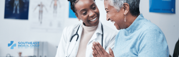 A smiling Black female doctor with a stethoscope interacts with a smiling older female patient. Southeast Medical Group logo is in the corner.