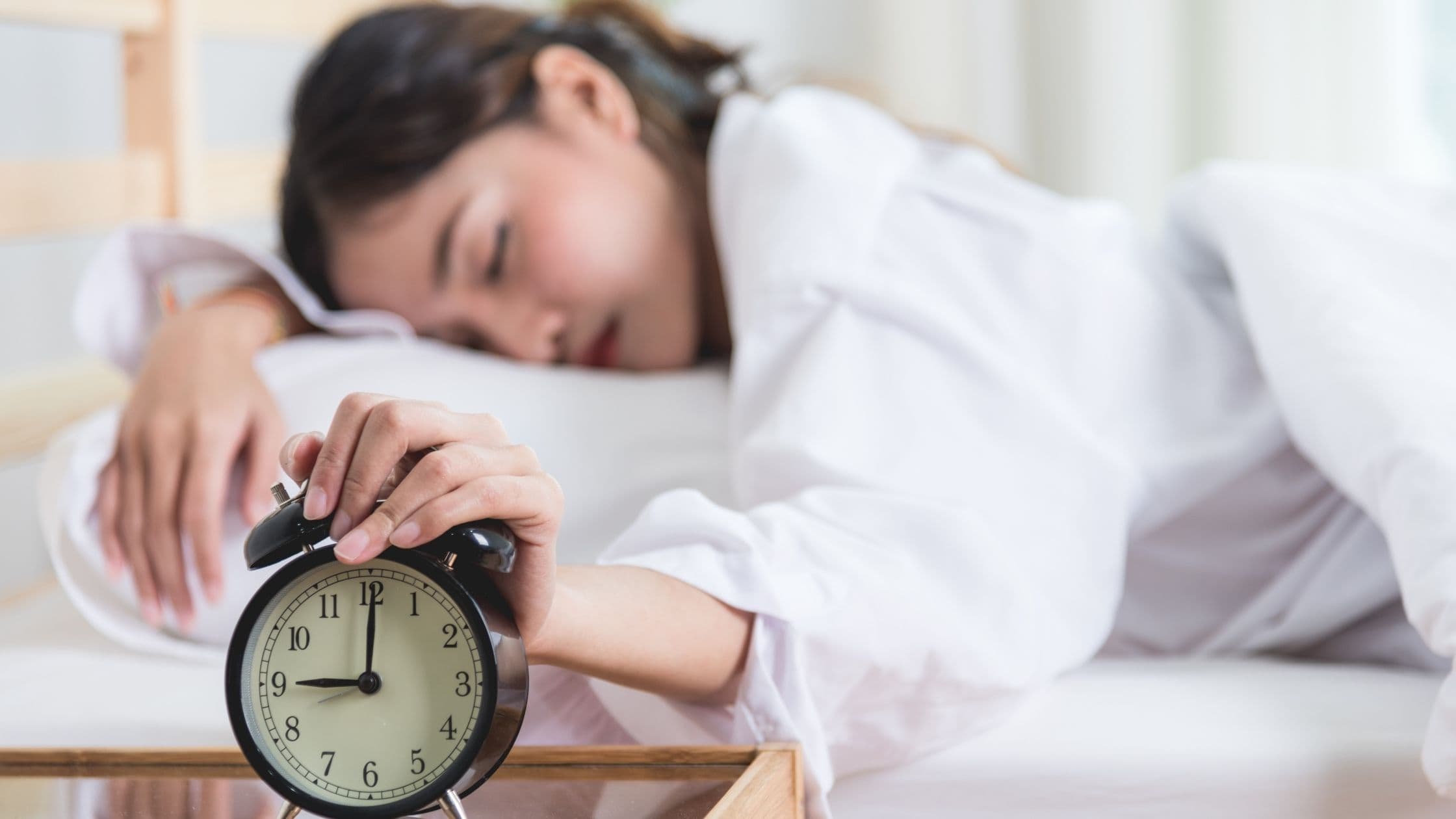 a woman is sleeping in bed while holding an alarm clock .
