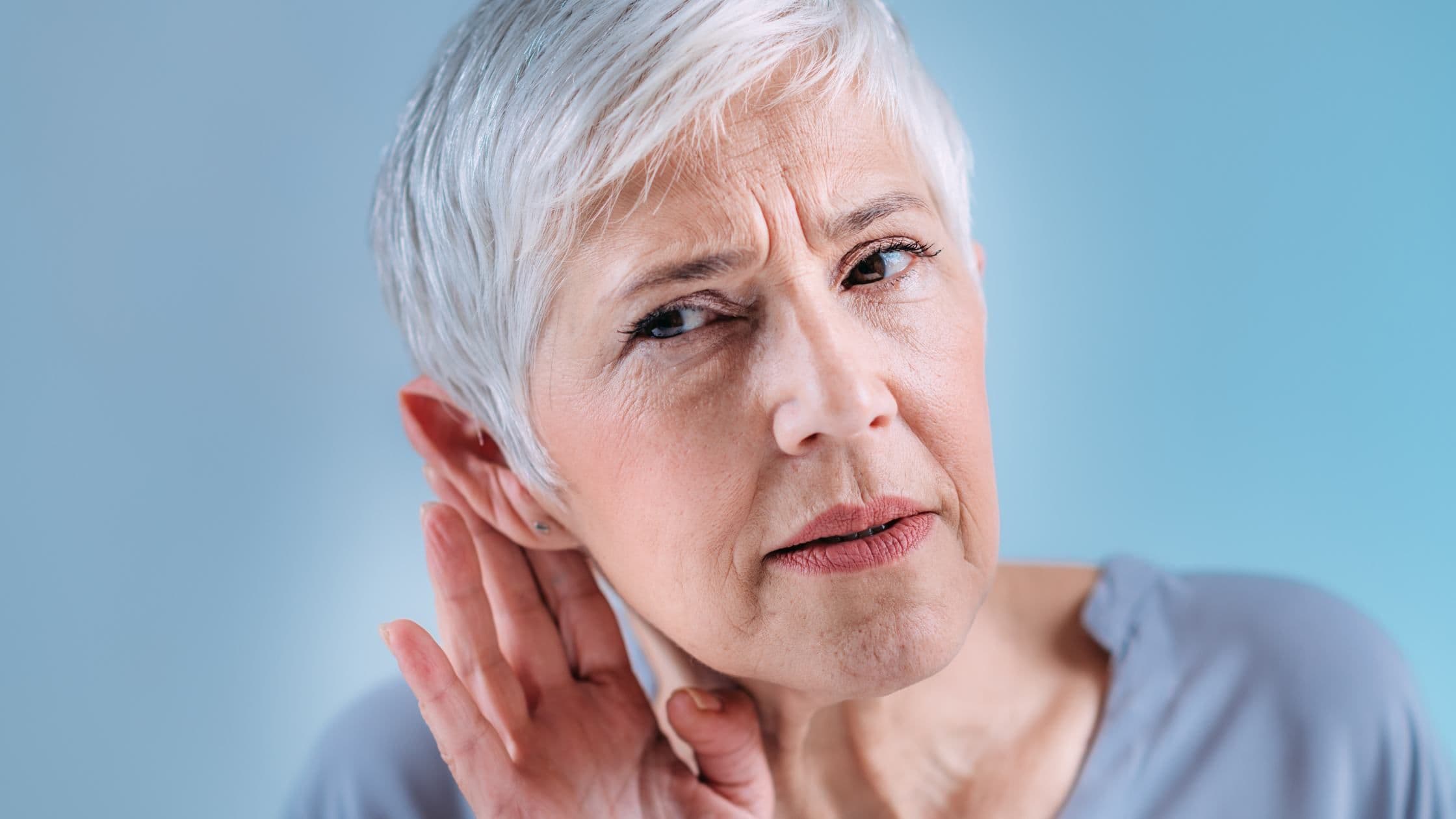 an elderly woman is holding her hand to her ear .