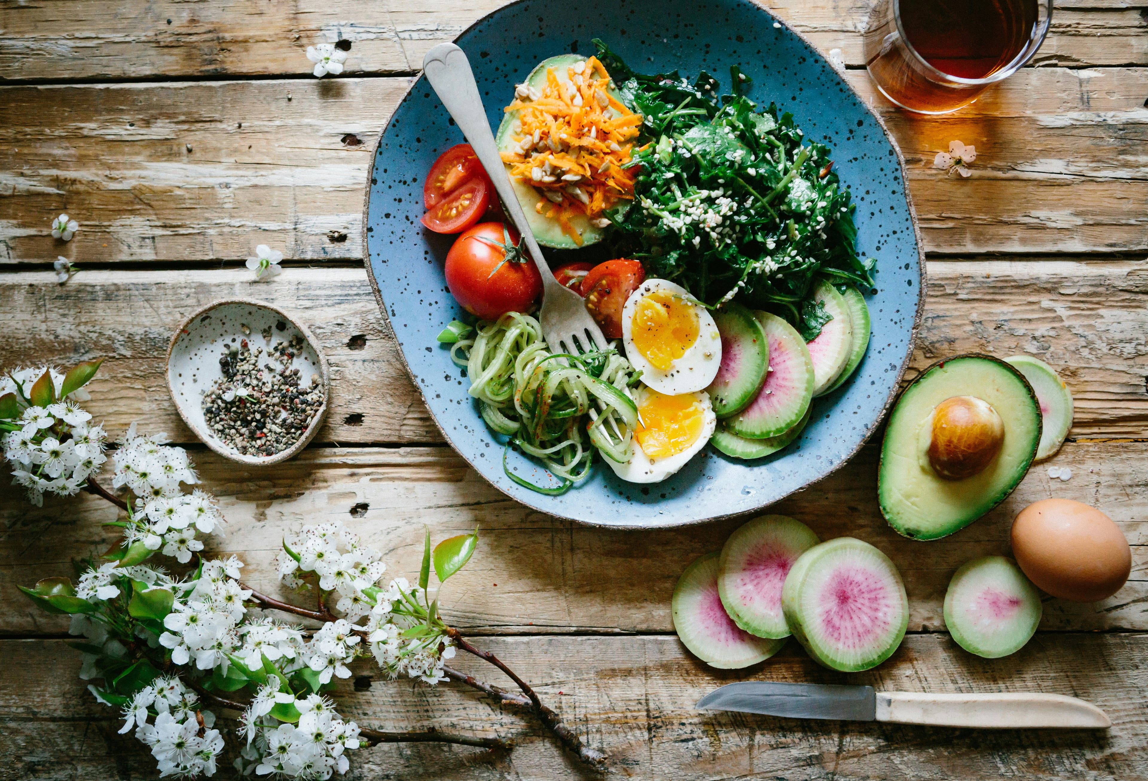 a plate of food with eggs , avocado , tomatoes and spinach on a wooden table .