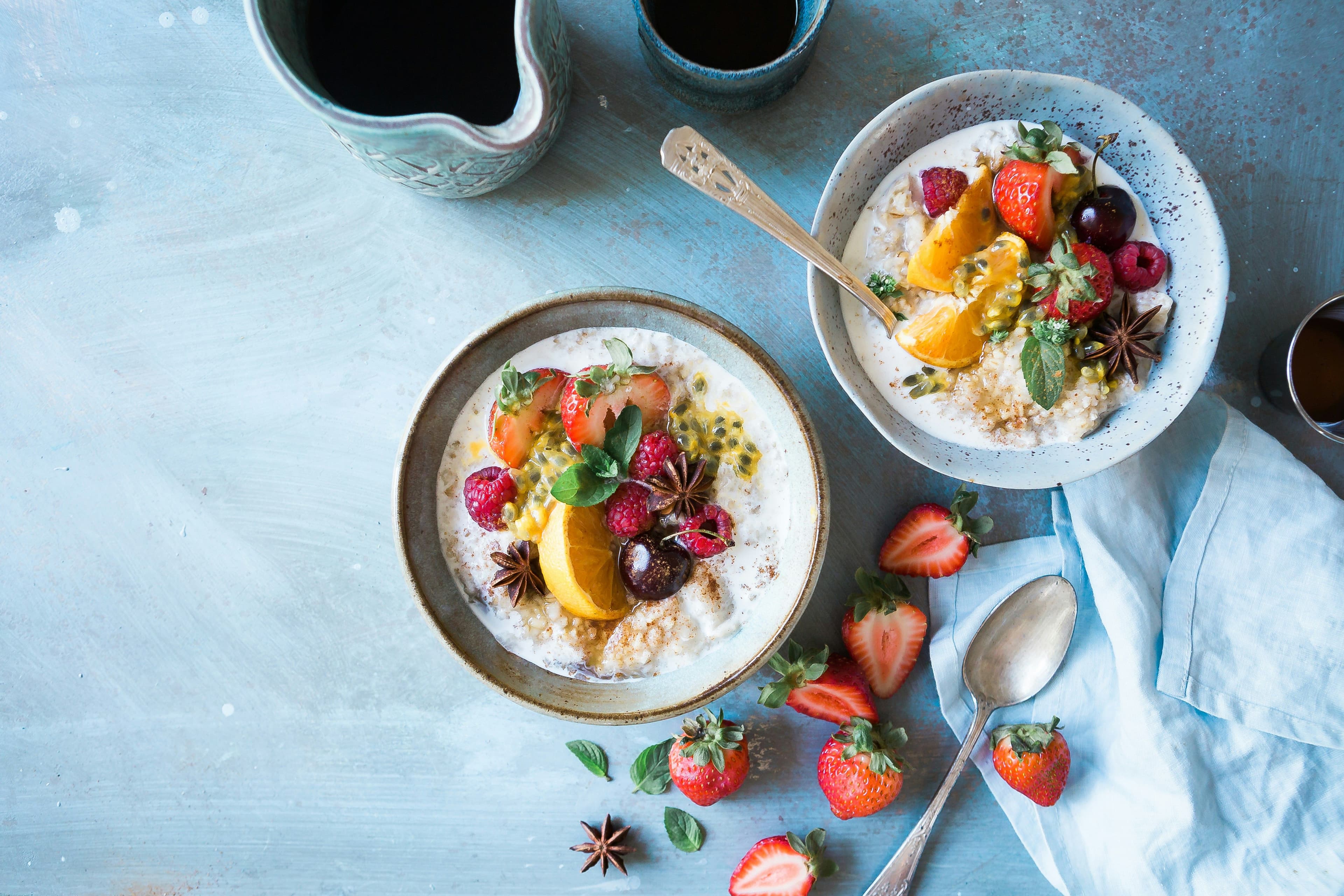 two bowls of oatmeal with fruit and a pitcher of coffee on a table .