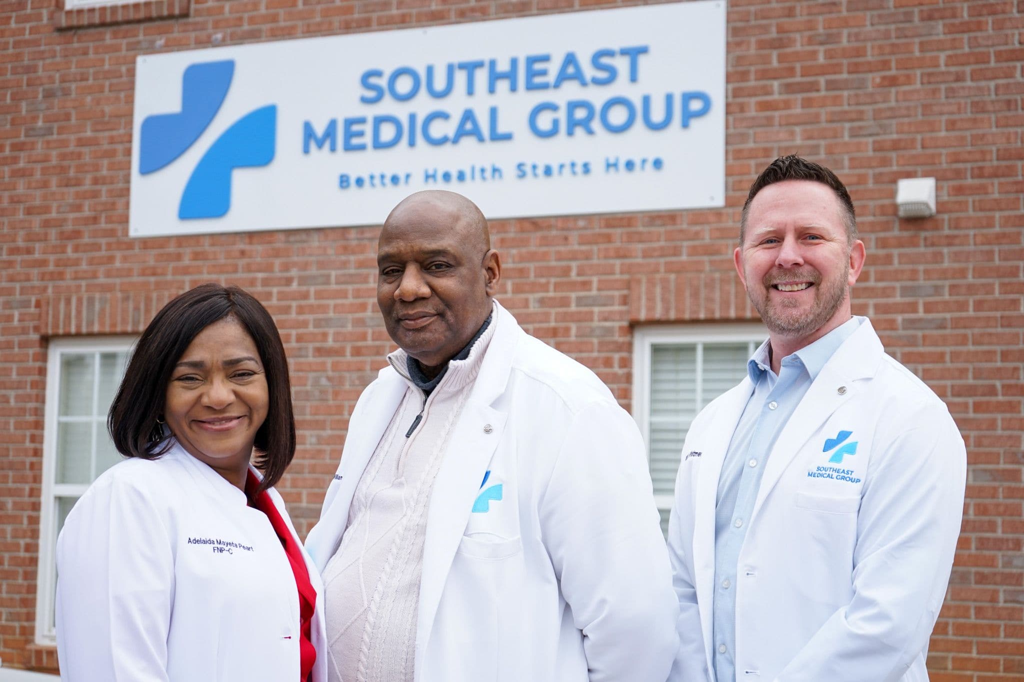 three doctors are posing for a picture in front of a southeast medical group building .