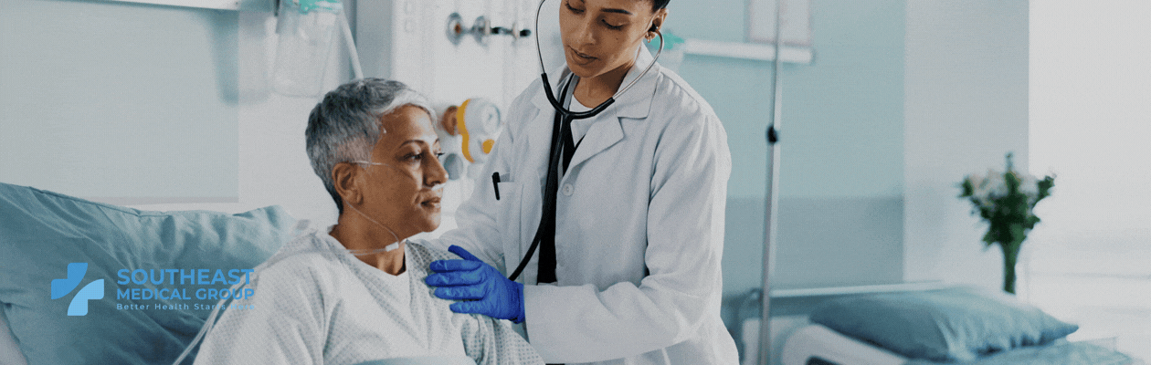 A doctor uses a stethoscope to examine an older patient wearing a nasal cannula in a hospital bed.