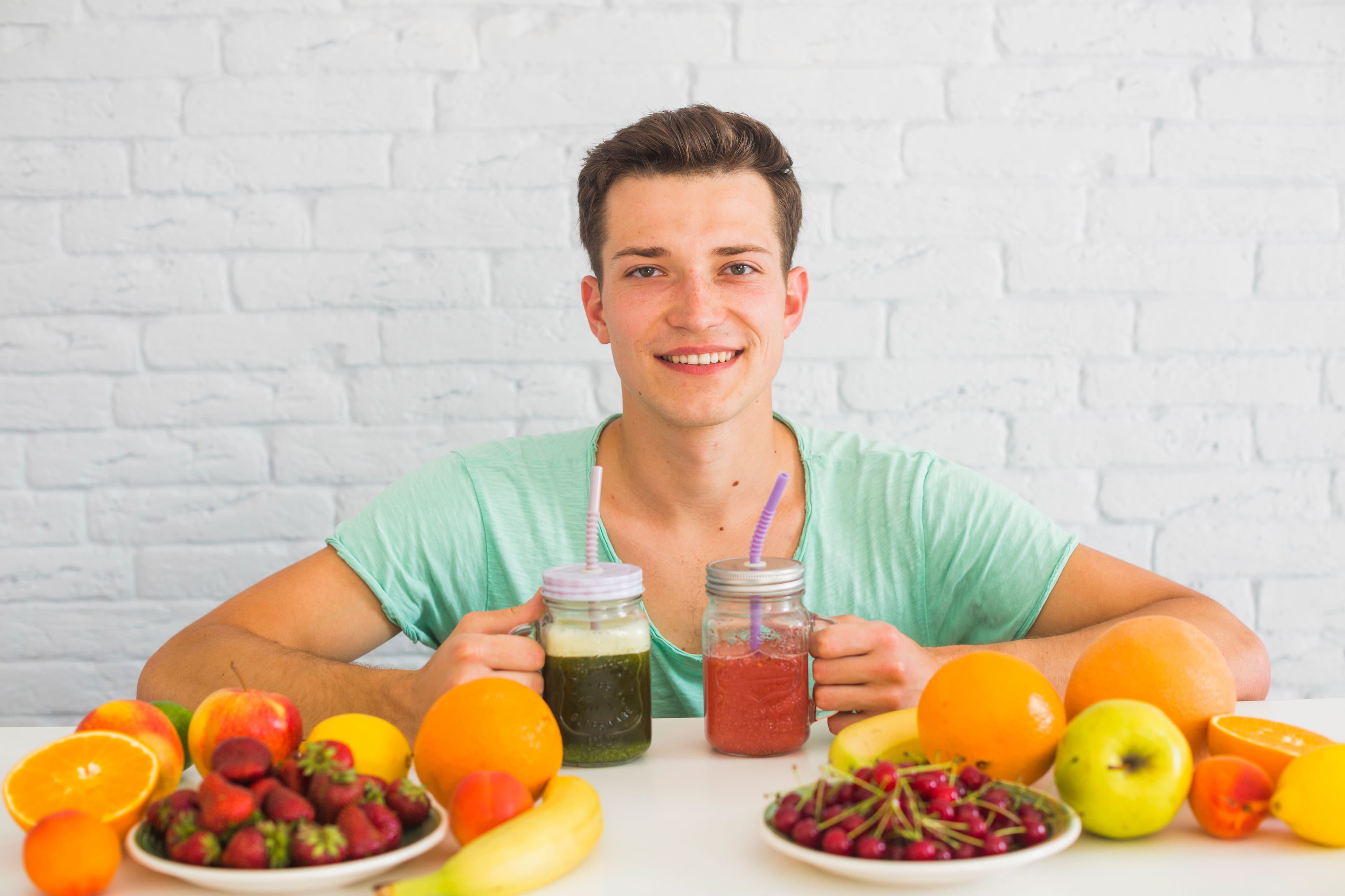a young man is sitting at a table with plates of fruit and drinking smoothies .