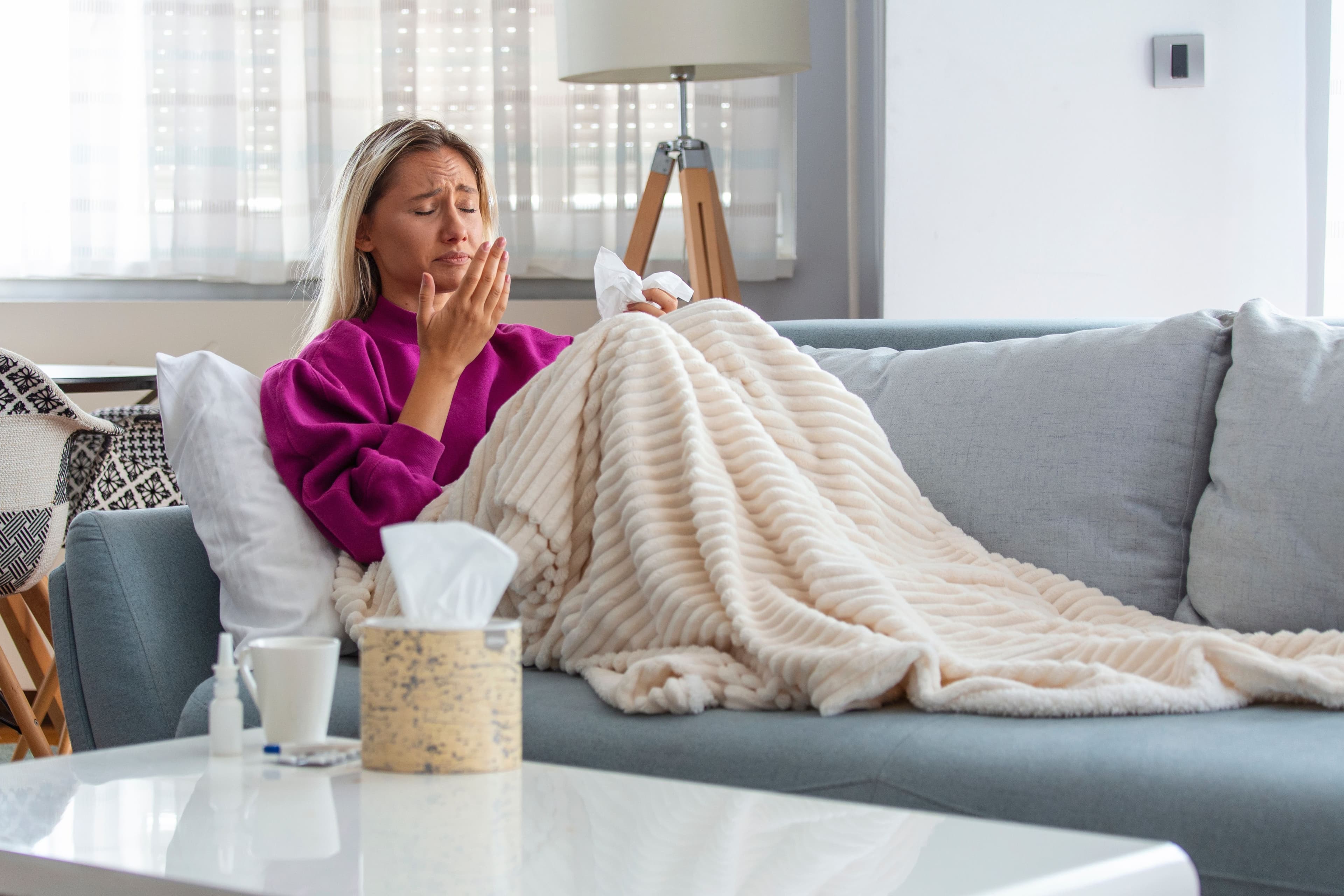 Flu: a woman is laying on a couch blowing her nose .