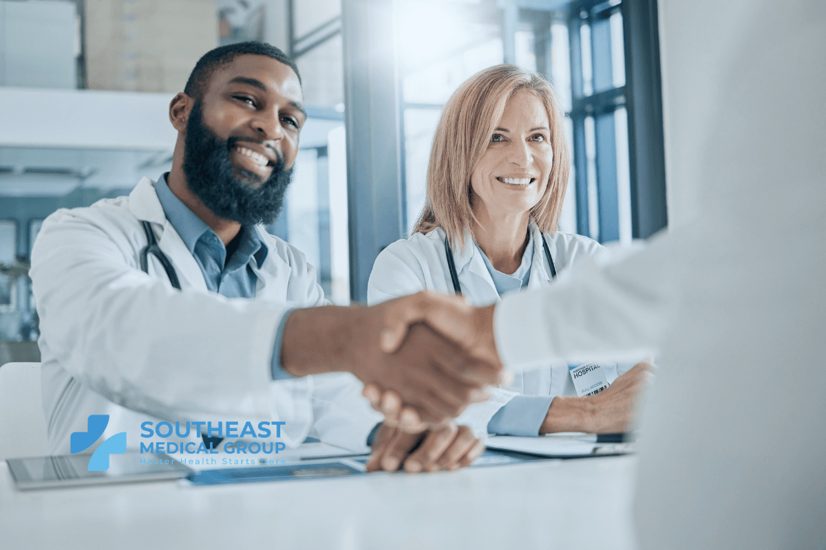 Smiling male and female doctors shaking hands with a person.