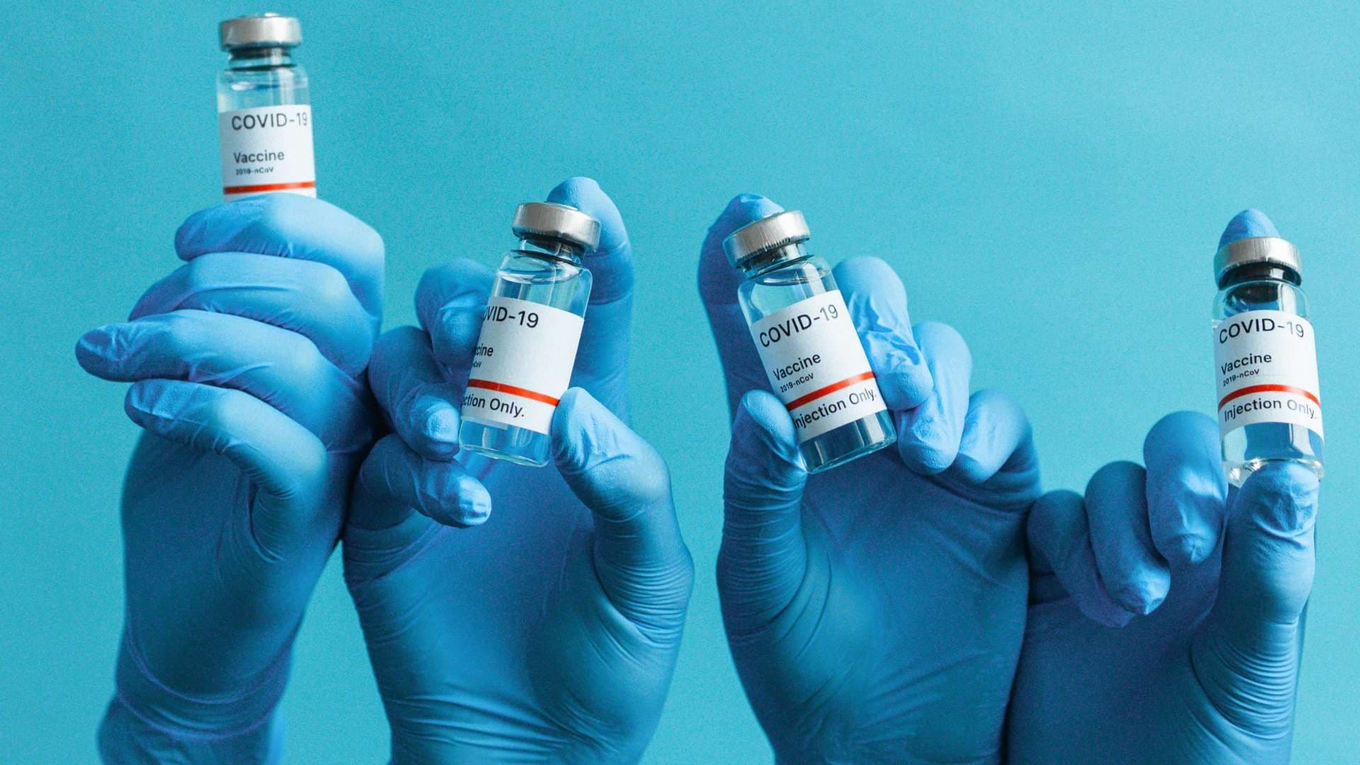 a person wearing blue gloves is holding four bottles of covid-19 vaccine .