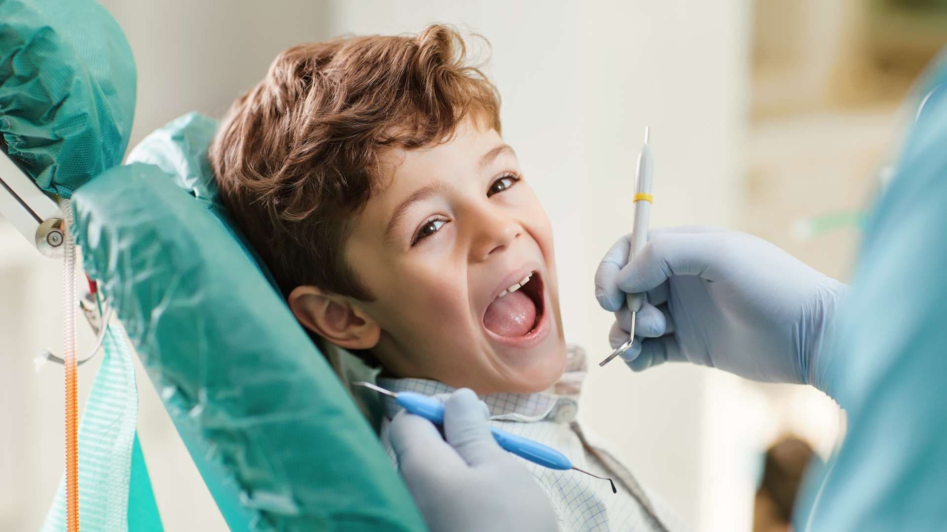 a young boy is sitting in a dental chair while a dentist examines his teeth .