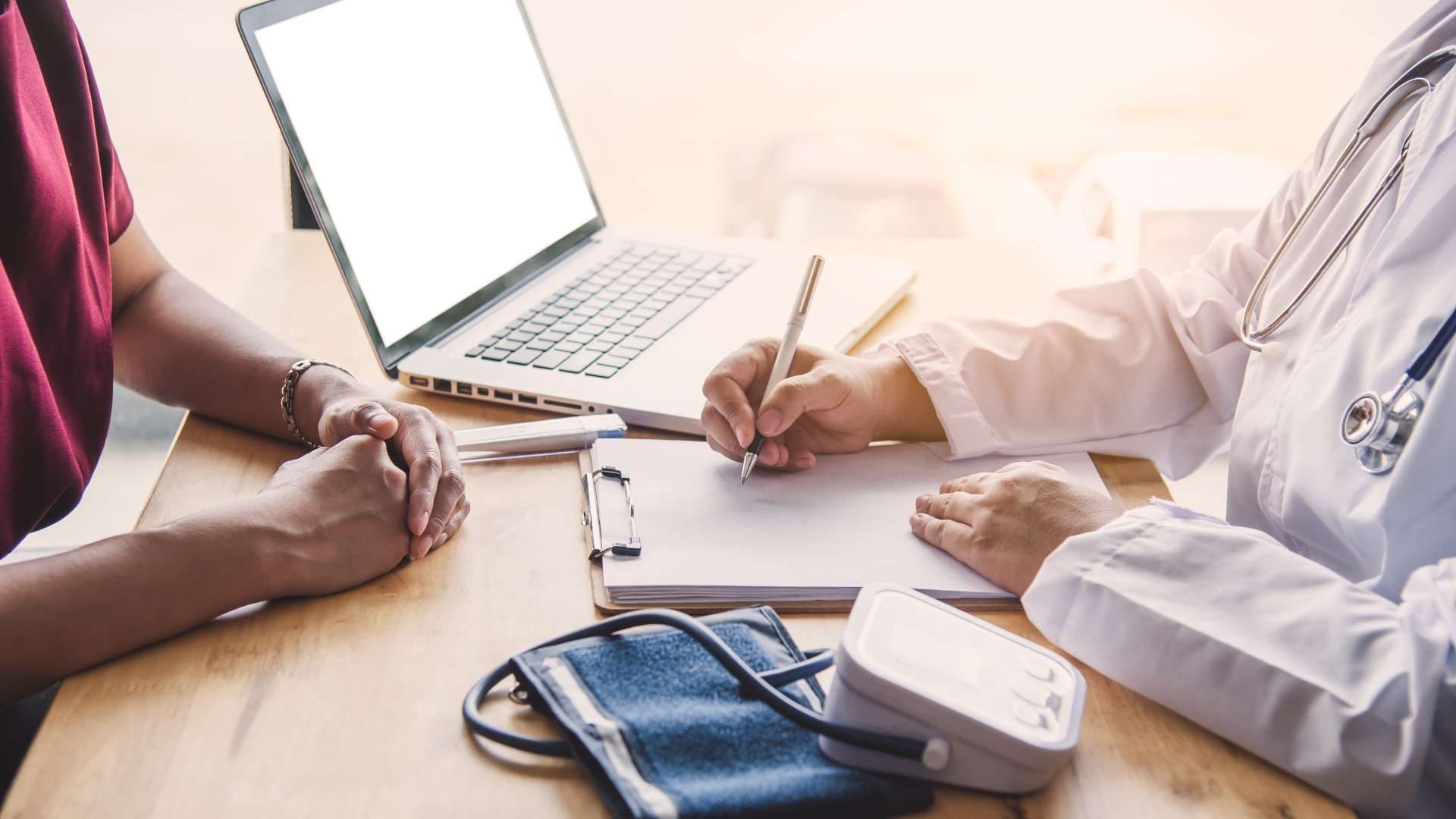 a doctor is sitting at a table with a patient and writing on a clipboard .